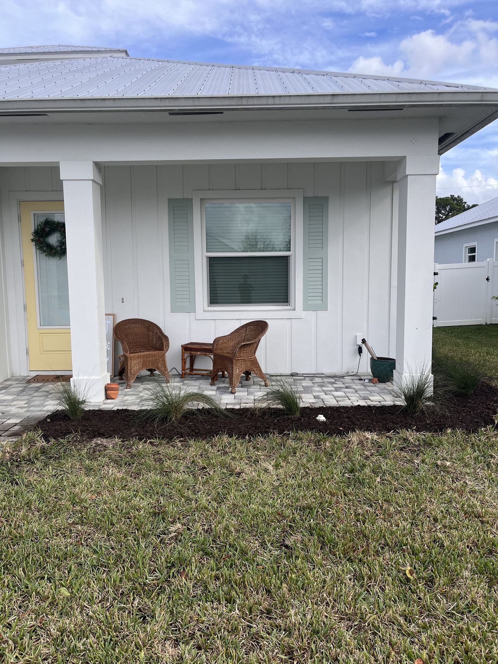 White cottage with metal roof, porch seating, and new landscape beds with ornamental grasses and mulch.